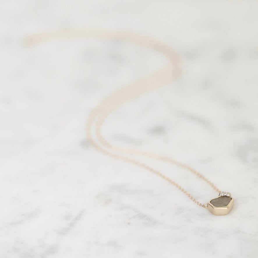 A delicate gold necklace with a small faceted geometric pendant resting on a light gray and white marble surface.