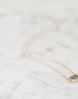 A delicate gold necklace with a small faceted geometric pendant resting on a light gray and white marble surface.