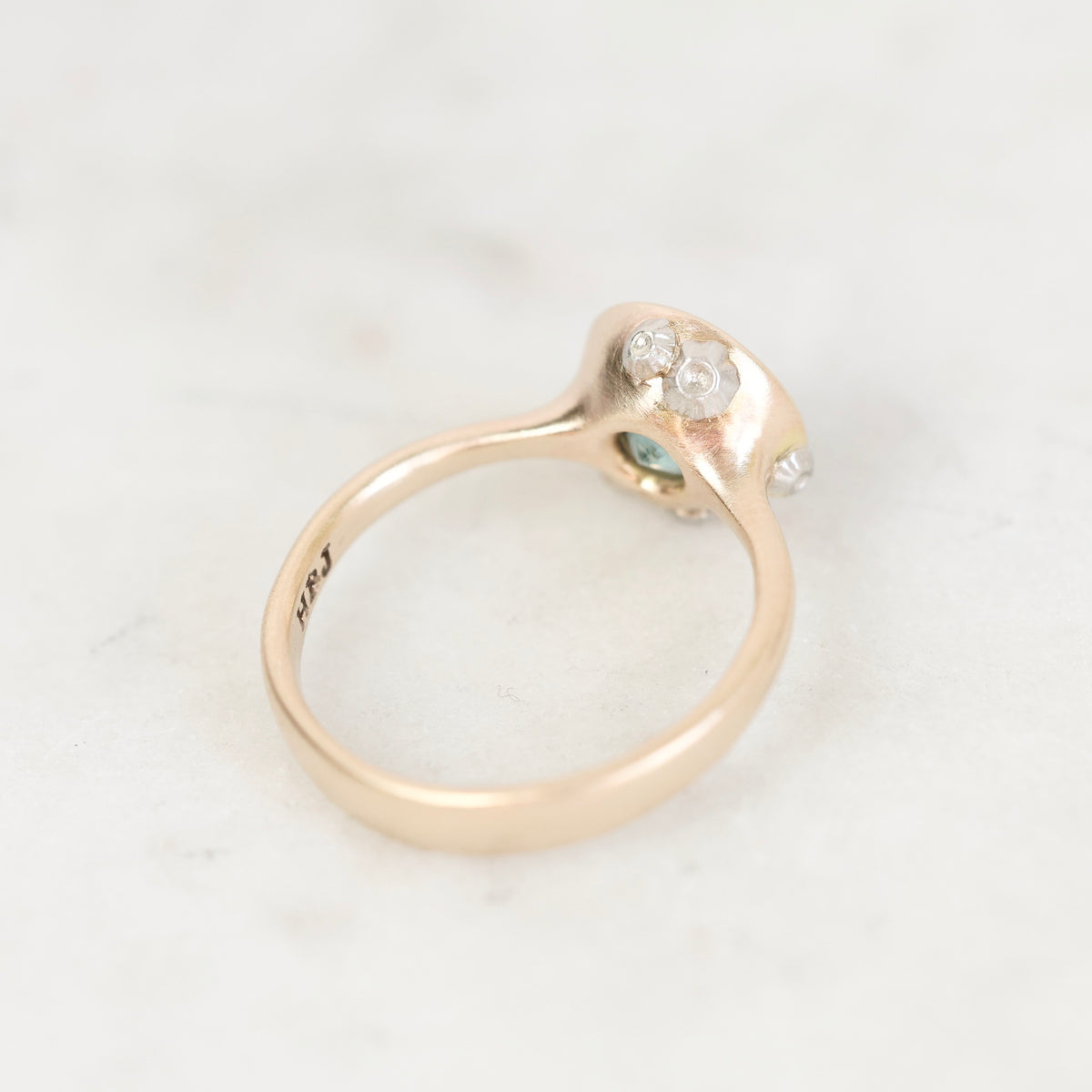 Ring facing away gold with bezel setting and platinum barnacle details against a plain background. 