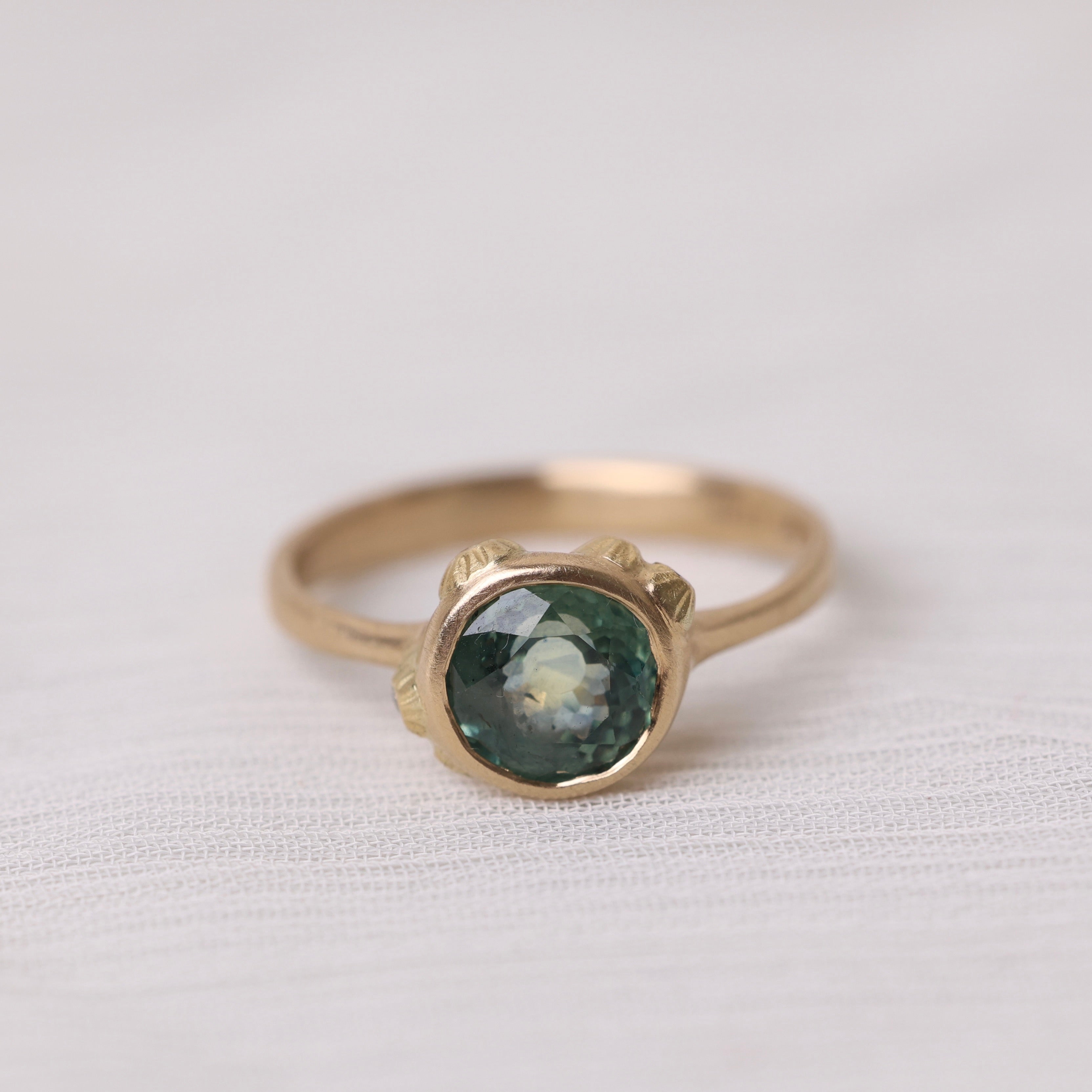 Gold ring with a green gemstone on a white fabric background