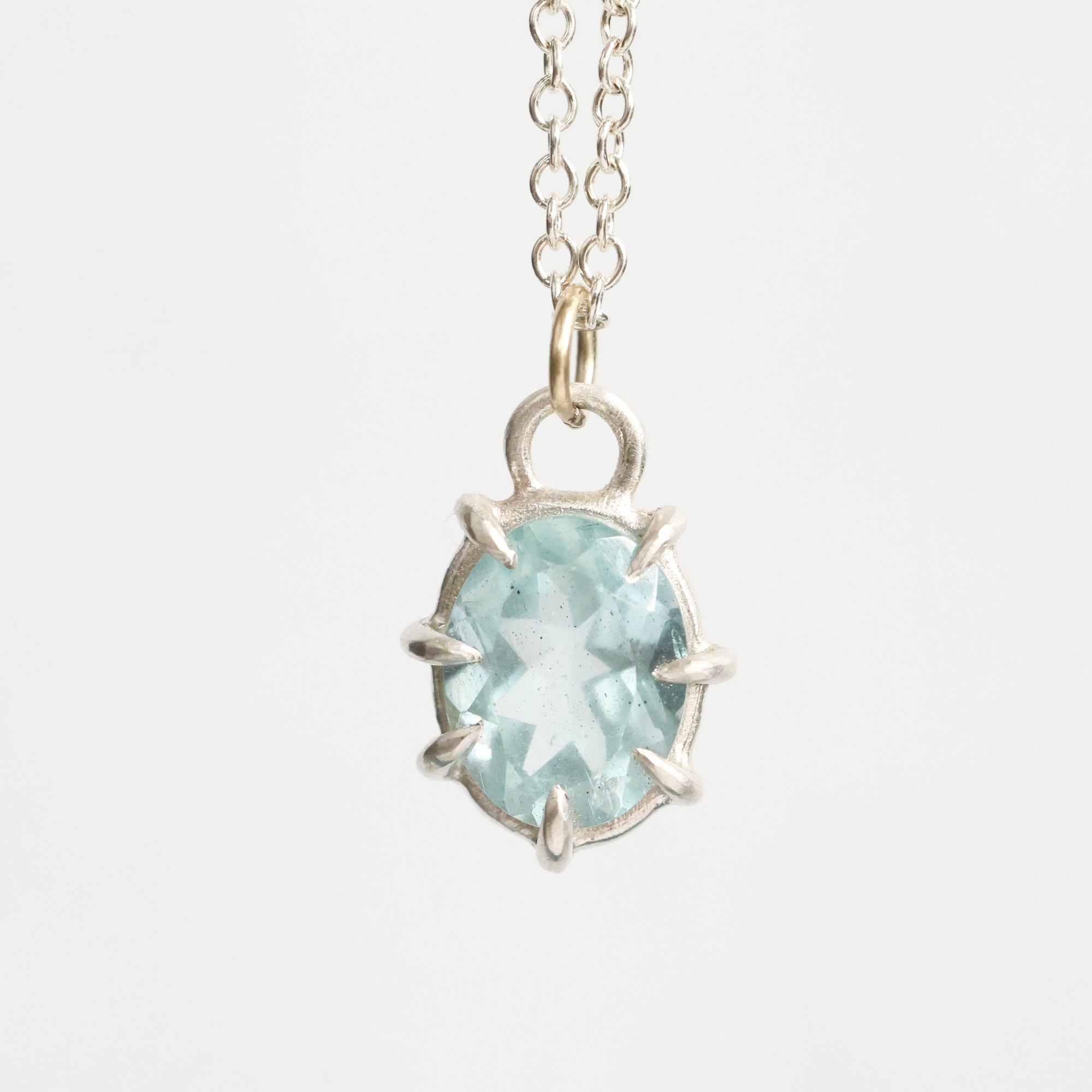 Silver necklace with a light blue gemstone pendant on a white background