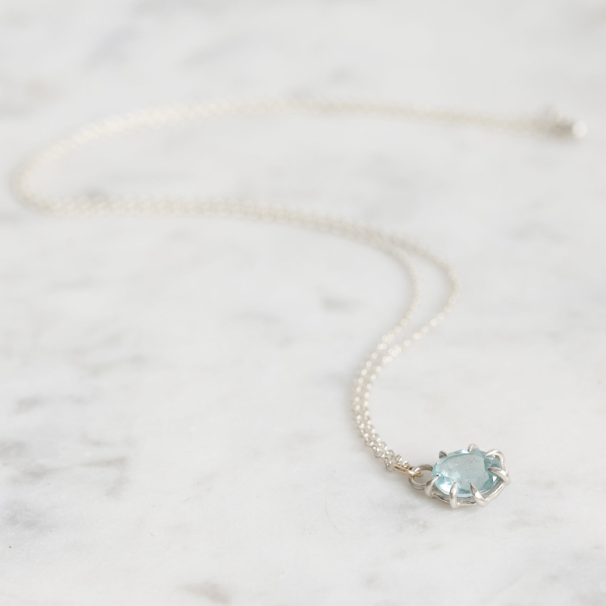 Necklace with a light blue gemstone on a marble surface