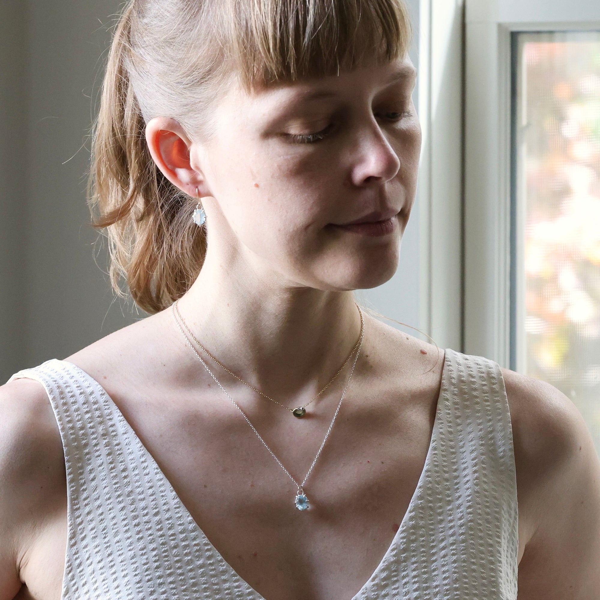 Woman wearing a necklace with a pendant in a softly lit room.