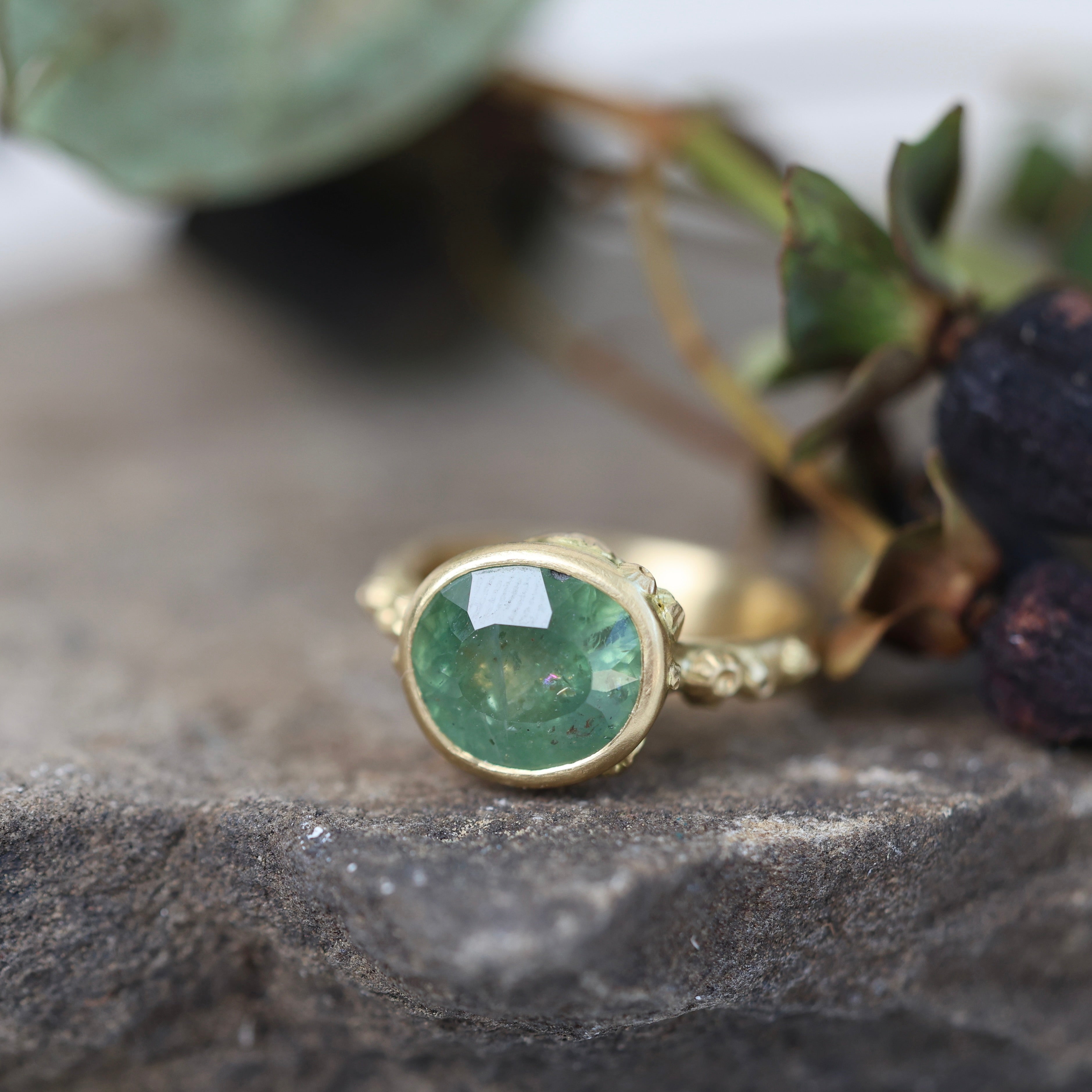 Gold ring with a green gemstone on a stone surface with leaves in the background