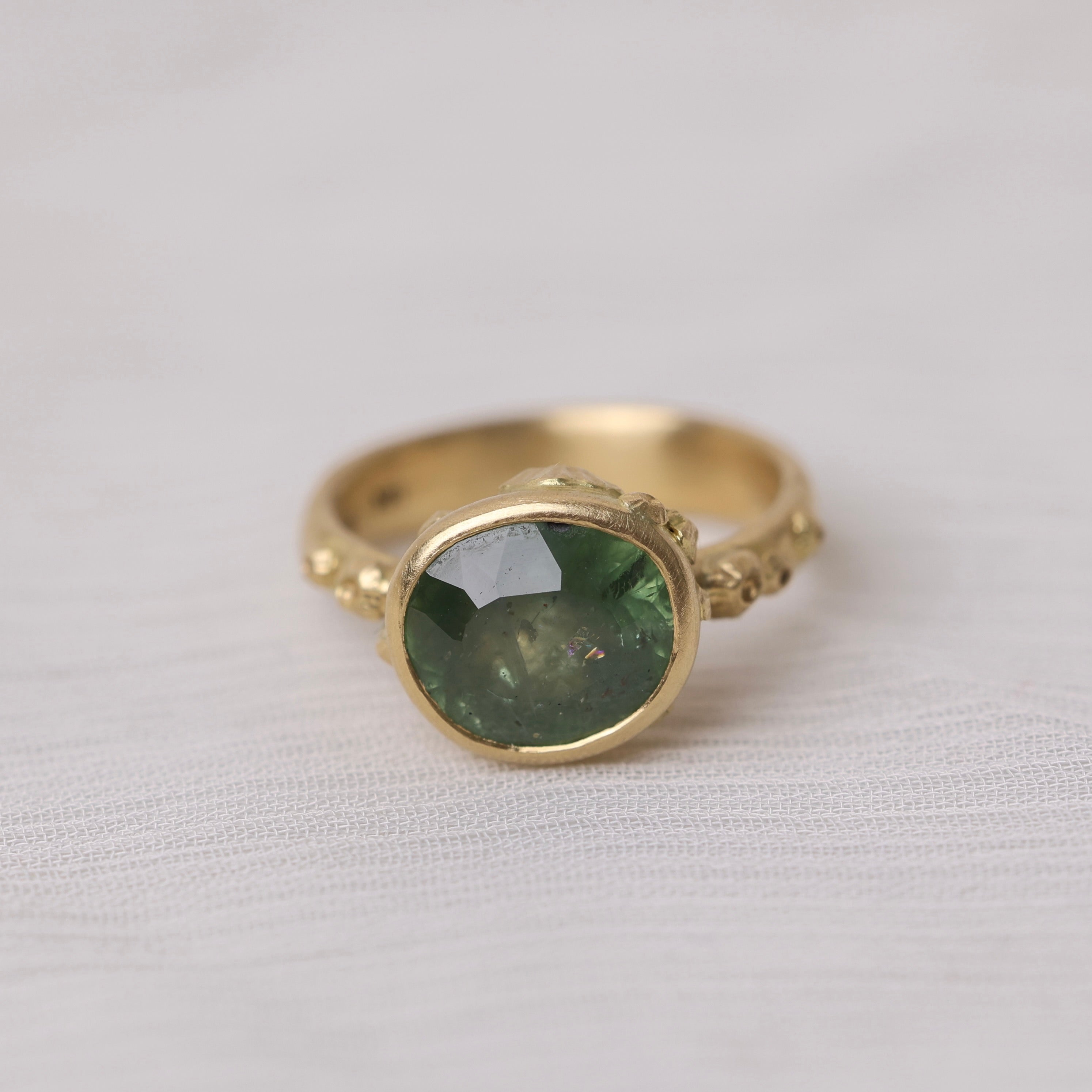 Gold ring with a green gemstone on a white fabric background