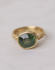 Gold ring with a green gemstone on a white fabric background