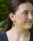 Green drop earrings on woman with brown hair. 