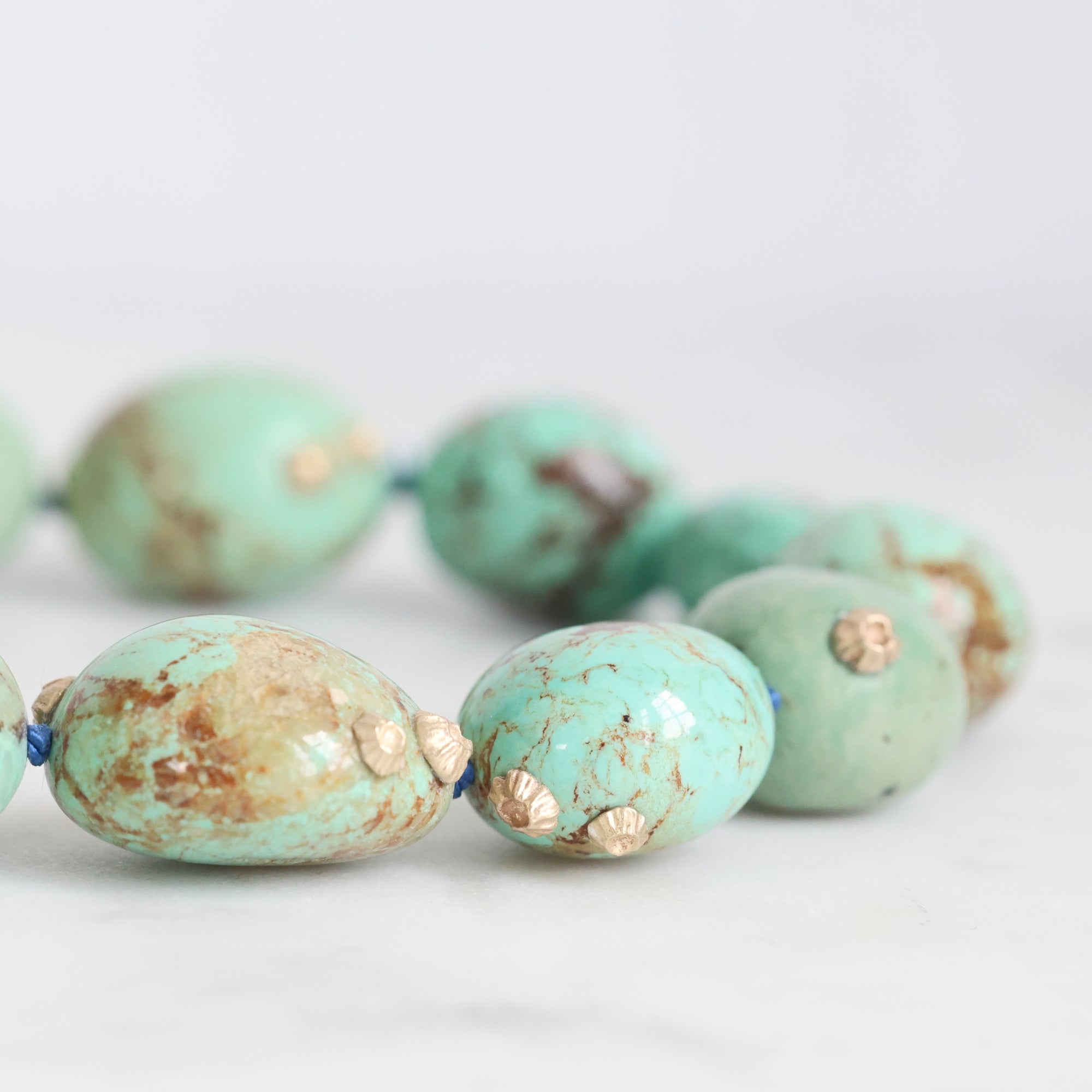 Turquoise beads with gold accents on a light gray background