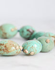 Turquoise beads with gold accents on a light gray background