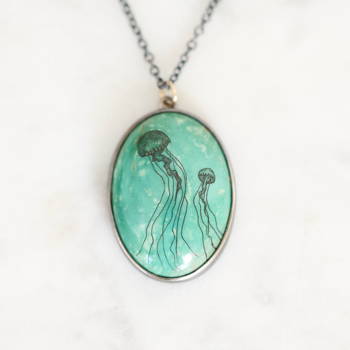 Necklace featuring a bezel set turquoise in oxidized silver. The turquoise features two jellyfish engravings. 