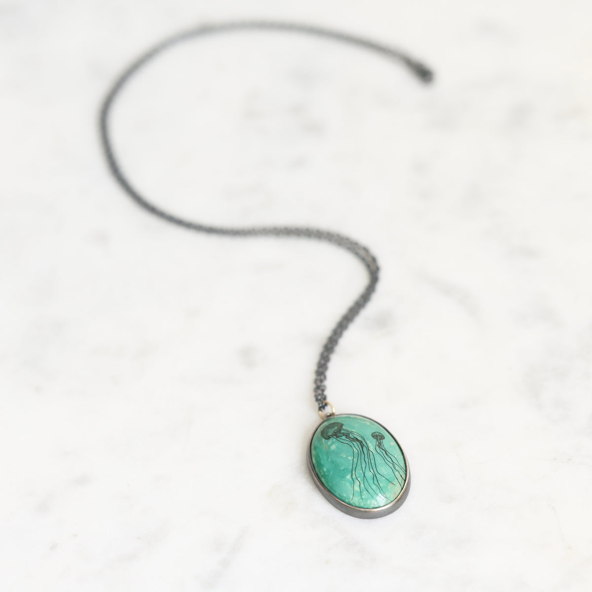 Necklace featuring a bezel set turquoise in oxidized silver. The turquoise features two jellyfish engravings. 