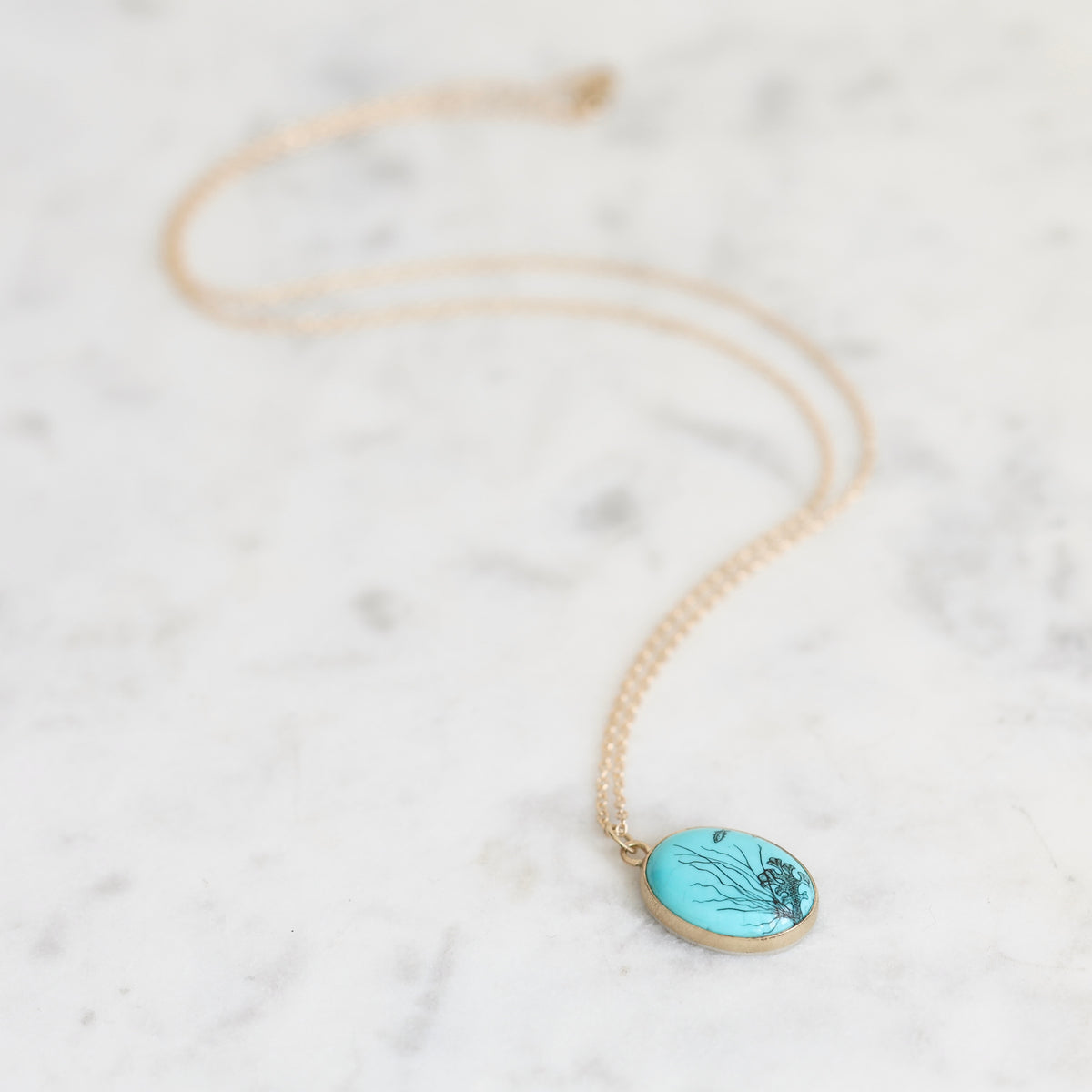 Necklace with gold chain and turquoise pendant laid out. 