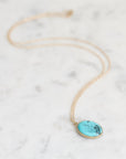 Necklace with gold chain and turquoise pendant laid out. 