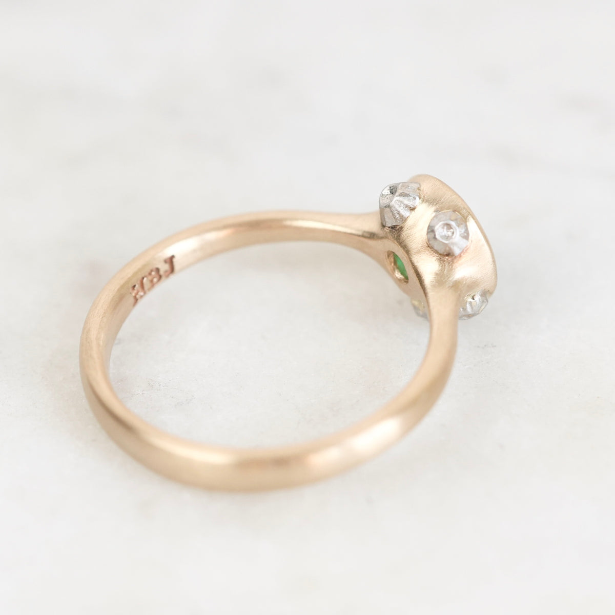 A vintage-style rose gold ring with a small cluster of clear gemstones on the setting, photographed on a light marble surface. The inside of the band shows a '10K' stamp.