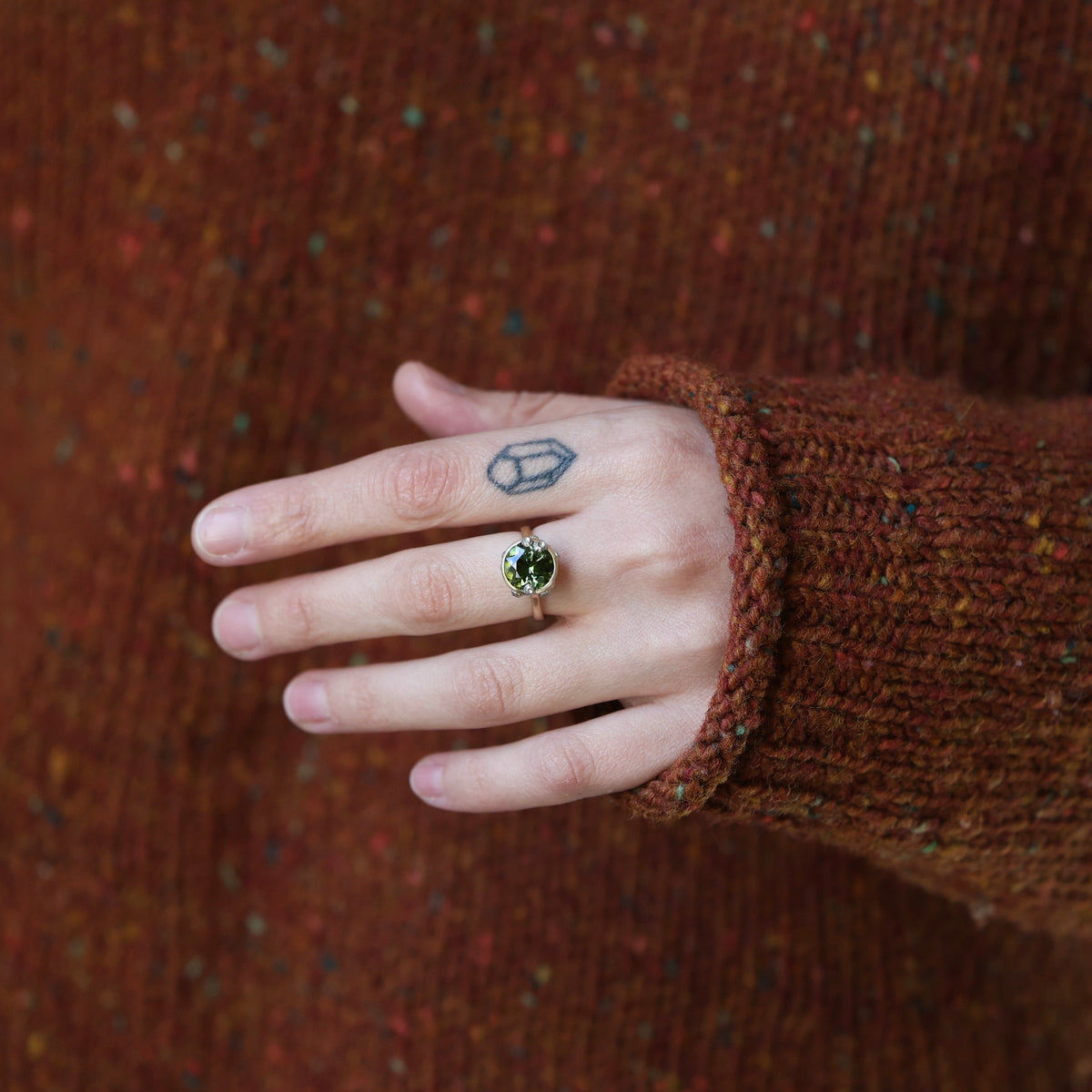 Hand wearing rust colored sweater and large green gemstone ring. 