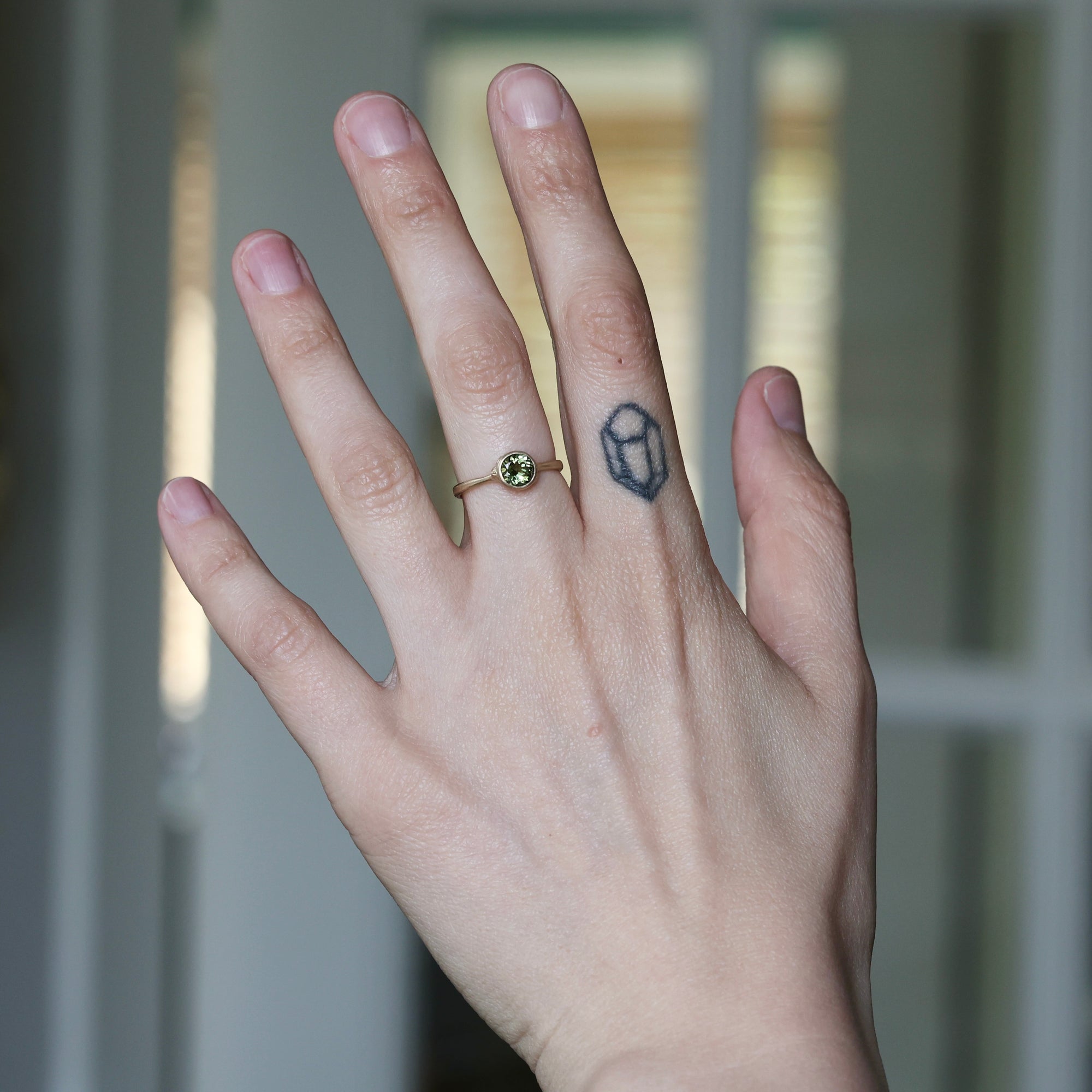Hand with a ring and a small tattoo on the finger against a blurred background