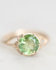 A round-cut light green gemstone ring set in a gold-toned prong setting on a soft white background.