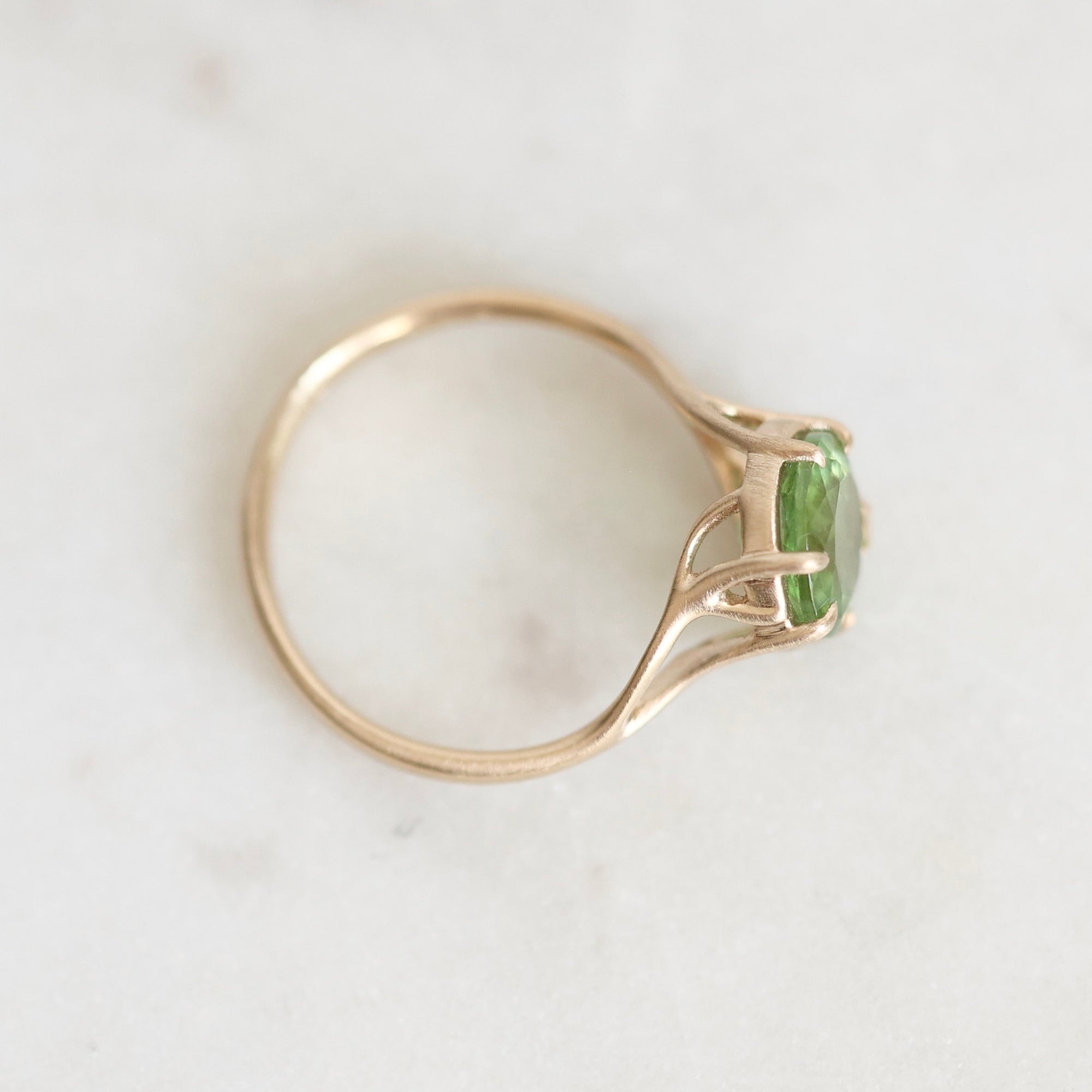 A gold ring with a green gemstone, photographed on a light marble surface.
