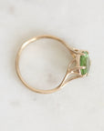 A gold ring with a green gemstone, photographed on a light marble surface.