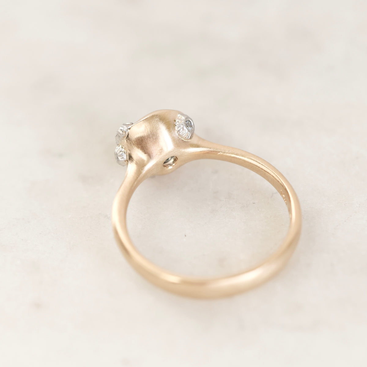 A gold ring with a unique sculptural dome-shaped setting featuring three small clear gemstones, photographed on a light marble surface.