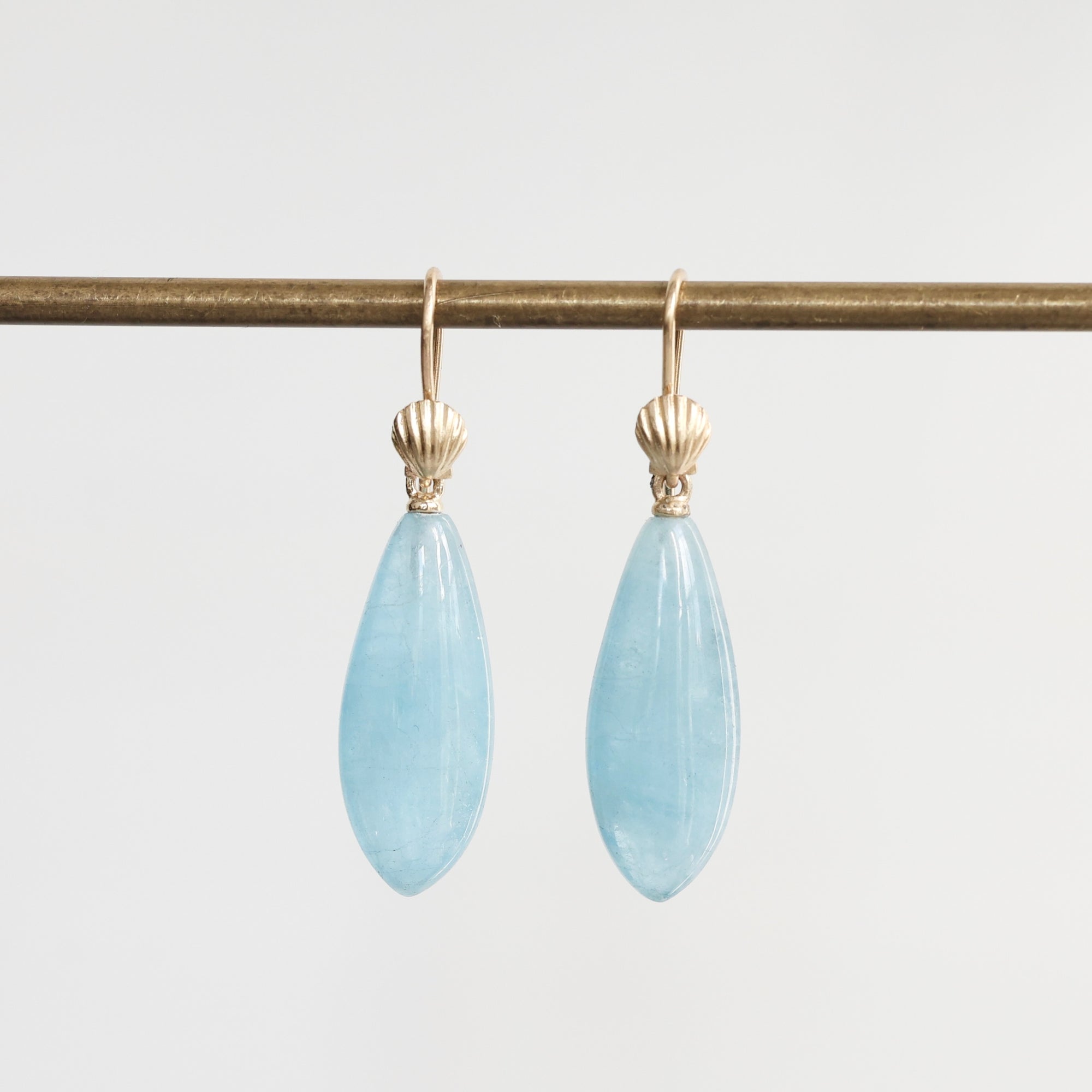 Pair of light blue teardrop earrings with gold hooks on a white background