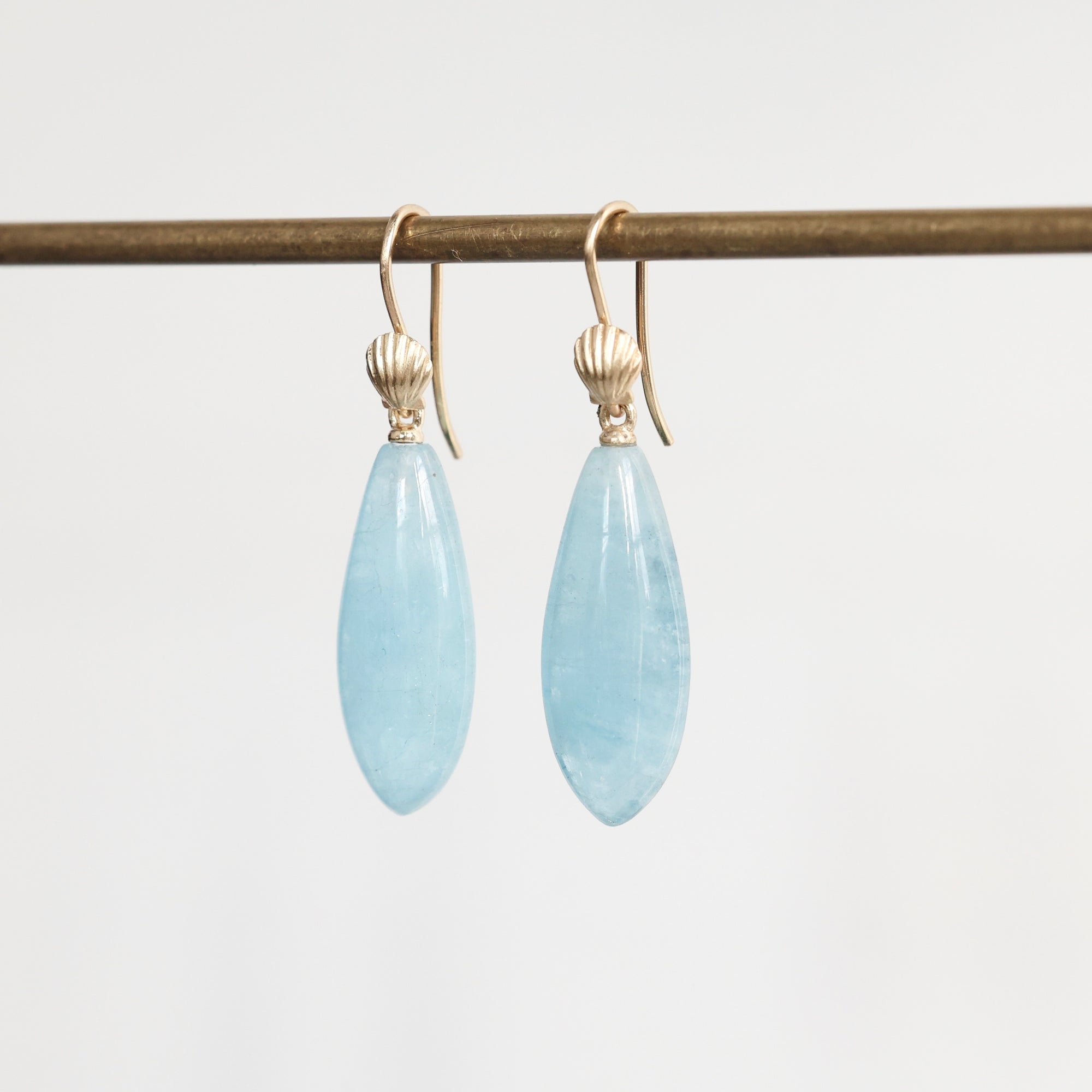 Pair of light blue teardrop earrings on gold hooks against a white background