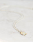 A delicate double-strand necklace with a small oval pendant featuring an iridescent white opal and gold-toned metal, resting on a light marble surface.