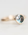 A close-up shot of a gold ring featuring a round light blue gemstone and three small clear accent stones, set against a soft, out-of-focus light background.