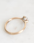 A close-up shot of a vintage-style ring with a gold band and a cluster of small clear gemstones on a light, off-white marble surface.