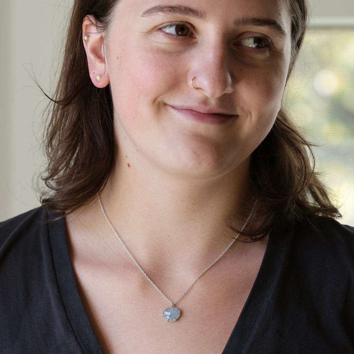 Woman wearing necklace with silver chain and aquamarine pendant against a neutral indoor background.