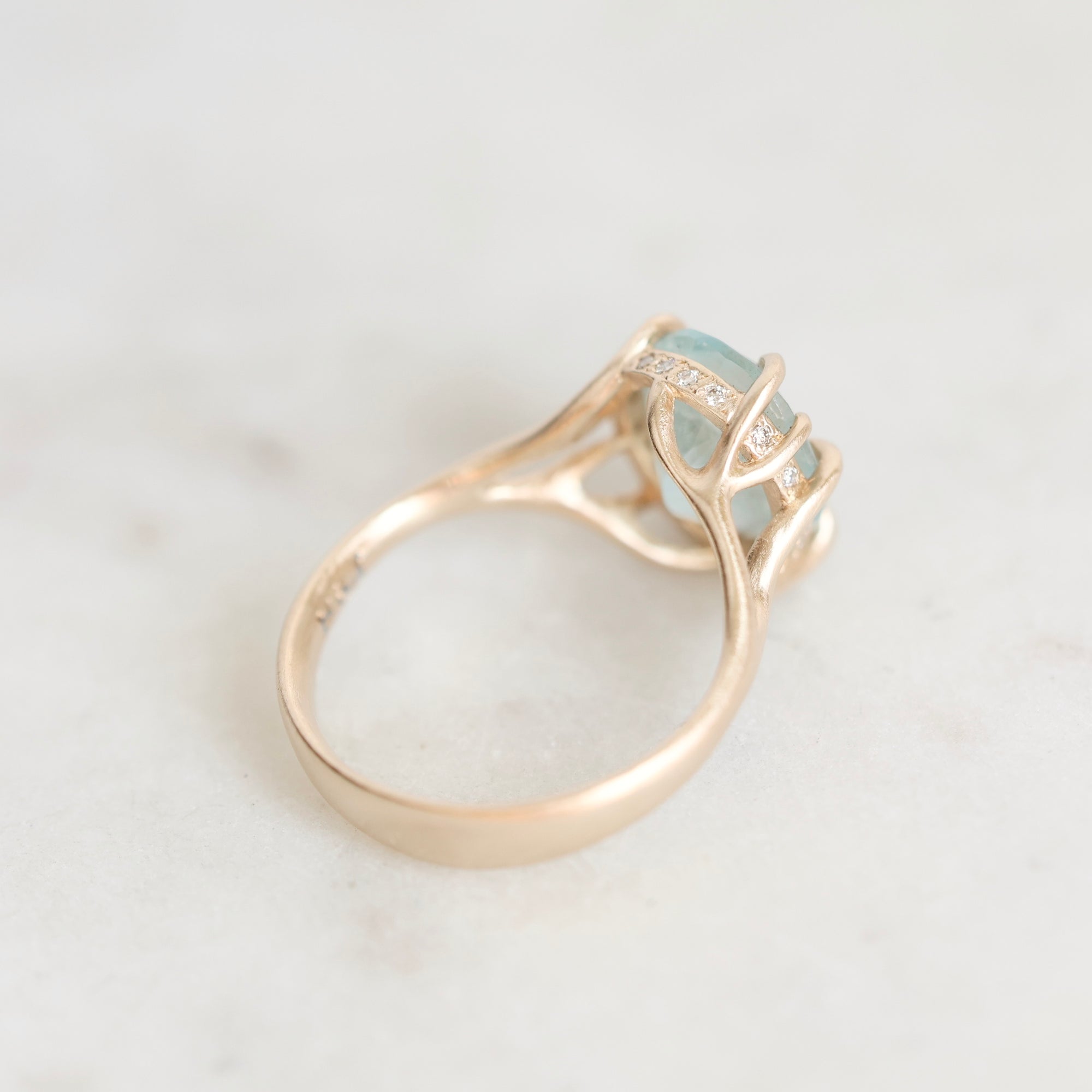 A rose gold ring with a light blue gemstone and small clear accent stones, photographed on a light marble surface.
