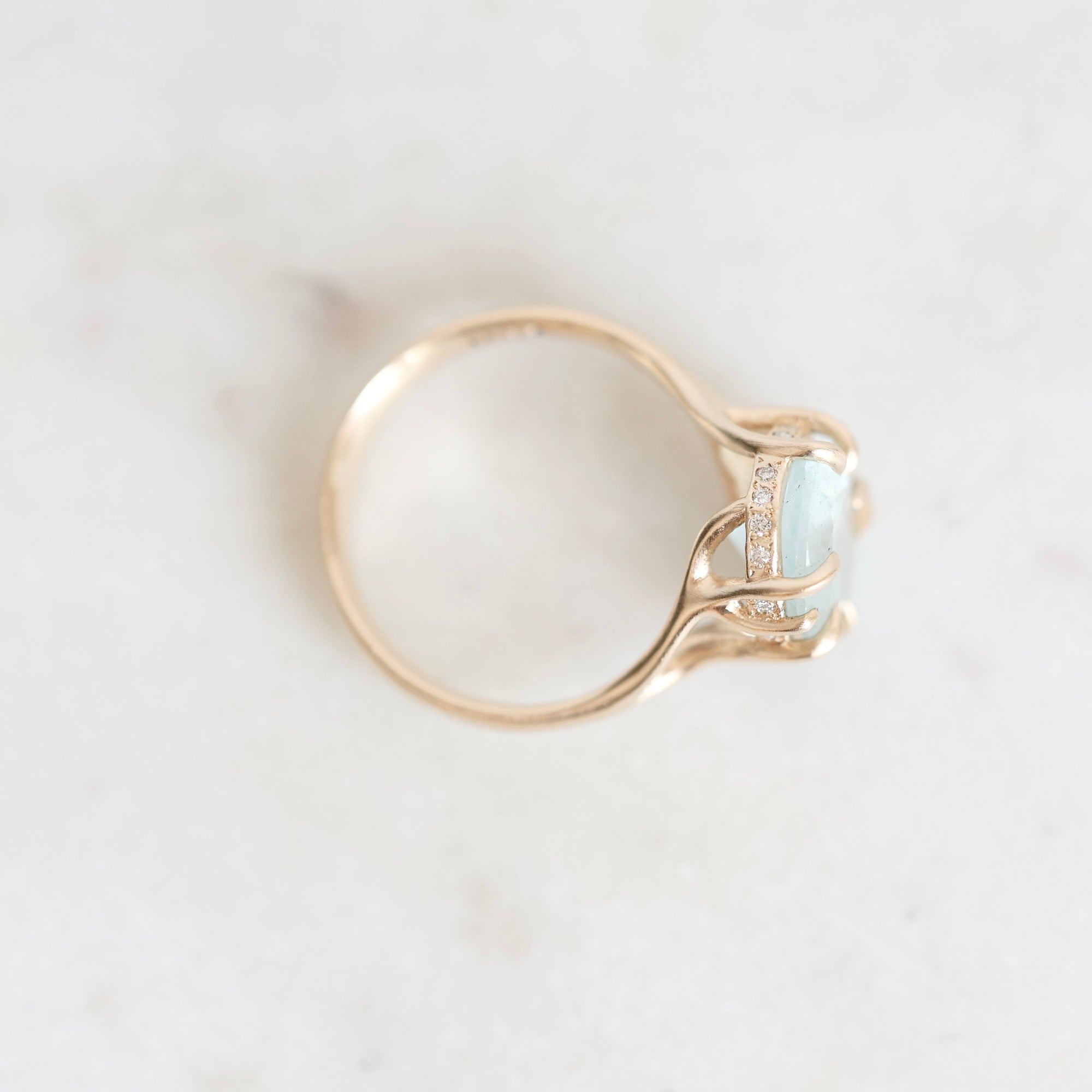 A gold ring with a light blue oval gemstone and small clear accent stones, photographed on a light marble surface.