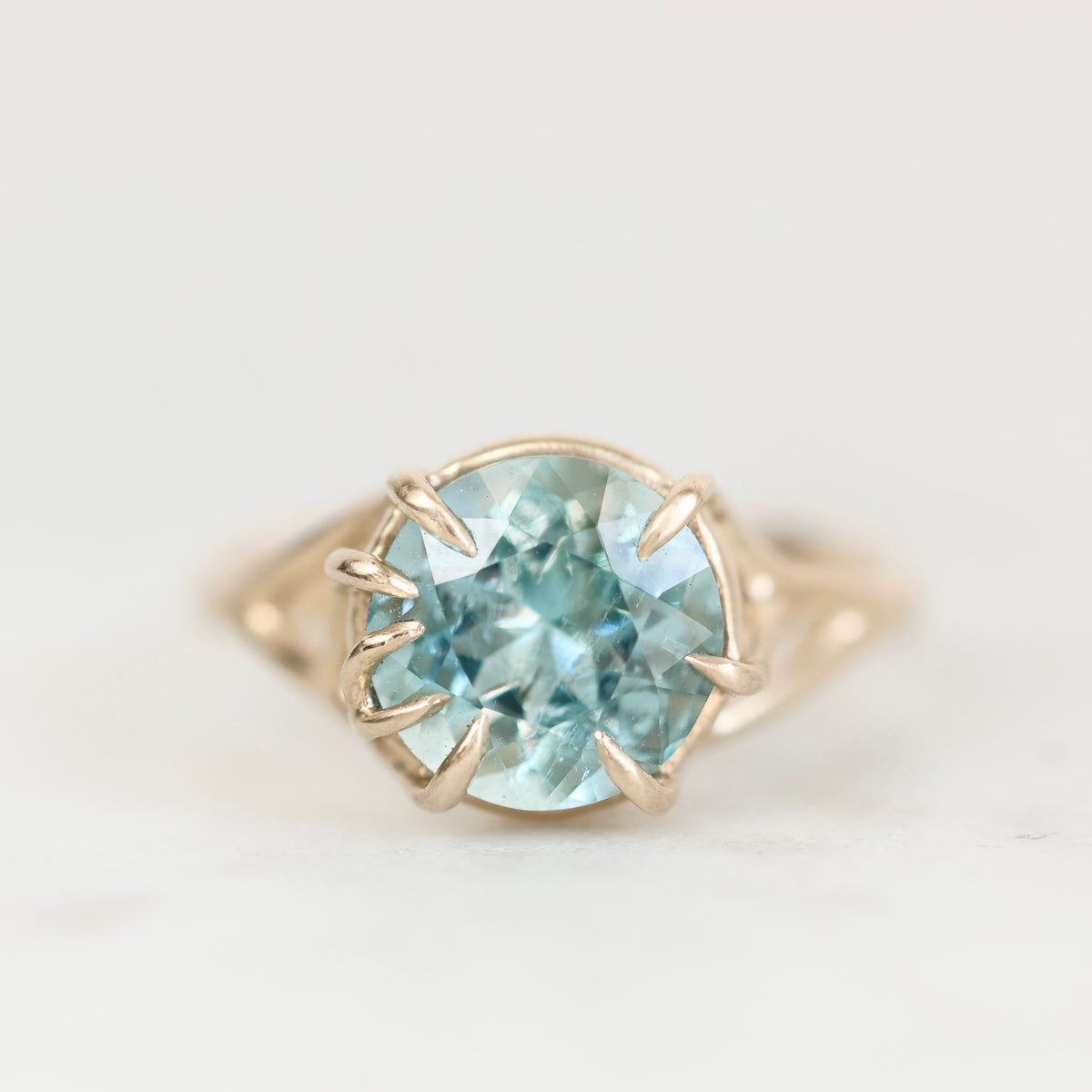 Blue gemstone ring with branchy prongs against a plain background. 
