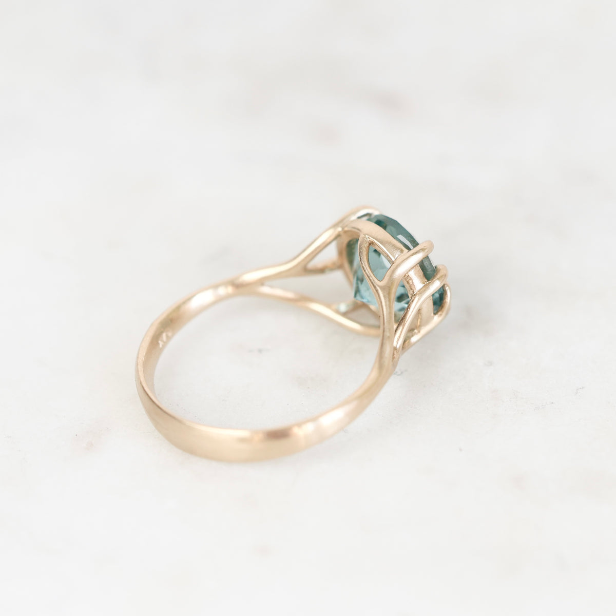 Ring turned away with gold branchy prong setting. Stone is blue background is white. 