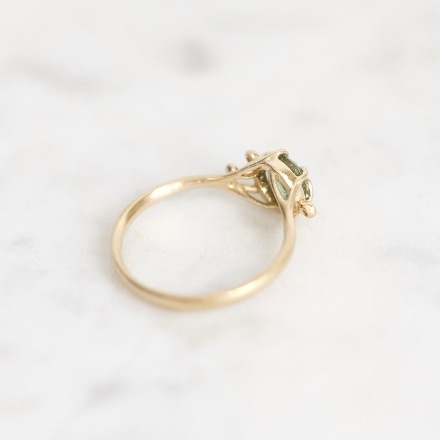 A yellow gold ring with a small cluster of green gemstones, photographed on a light marble surface.