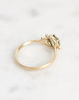 A yellow gold ring with a small cluster of green gemstones, photographed on a light marble surface.
