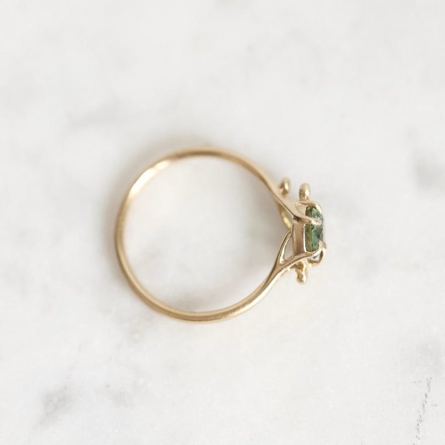 A gold ring with a small green gemstone, photographed on a light marble surface.