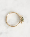 A gold ring with a small green gemstone, photographed on a light marble surface.