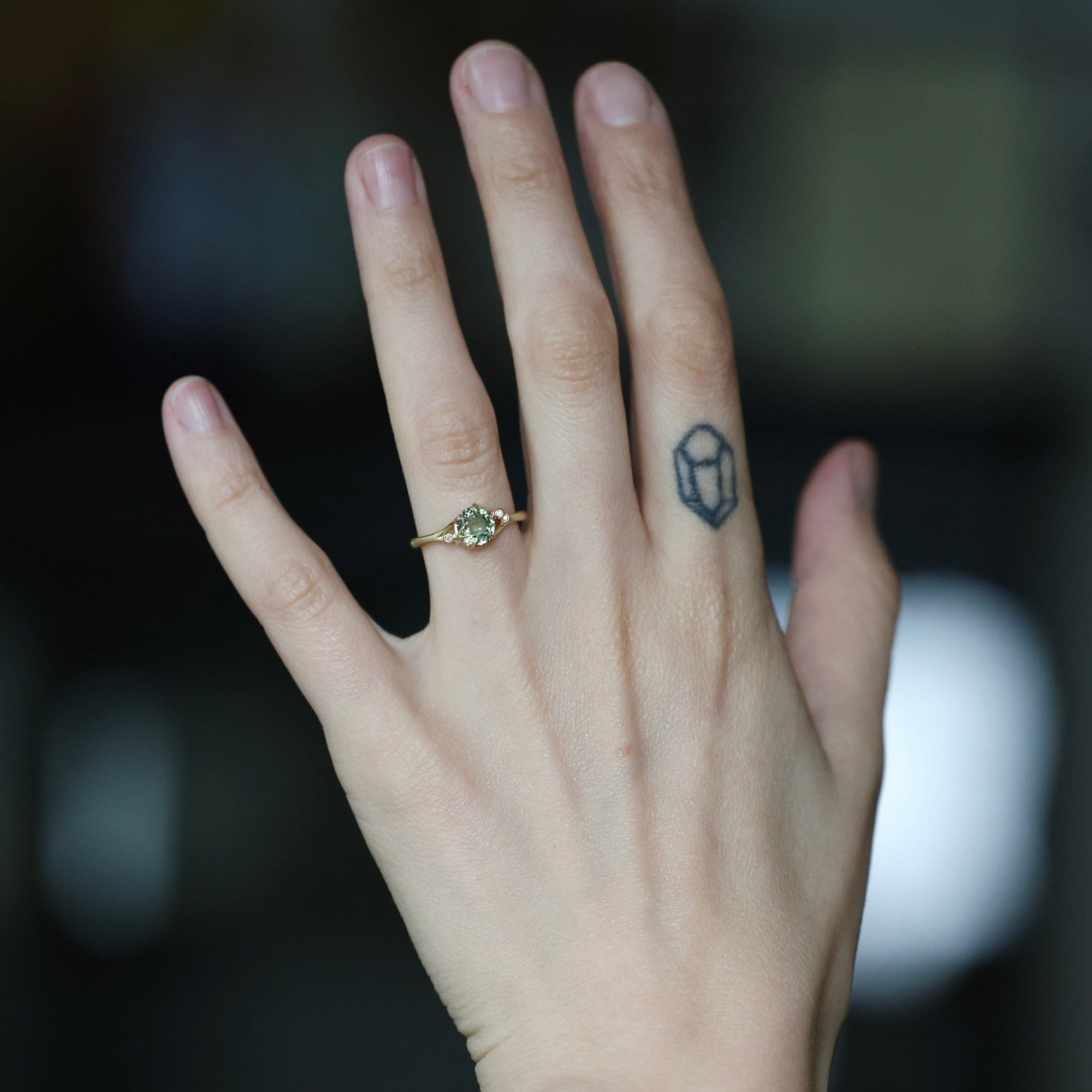 Green stone ring on hand with diamond berries. Hand has tattoo