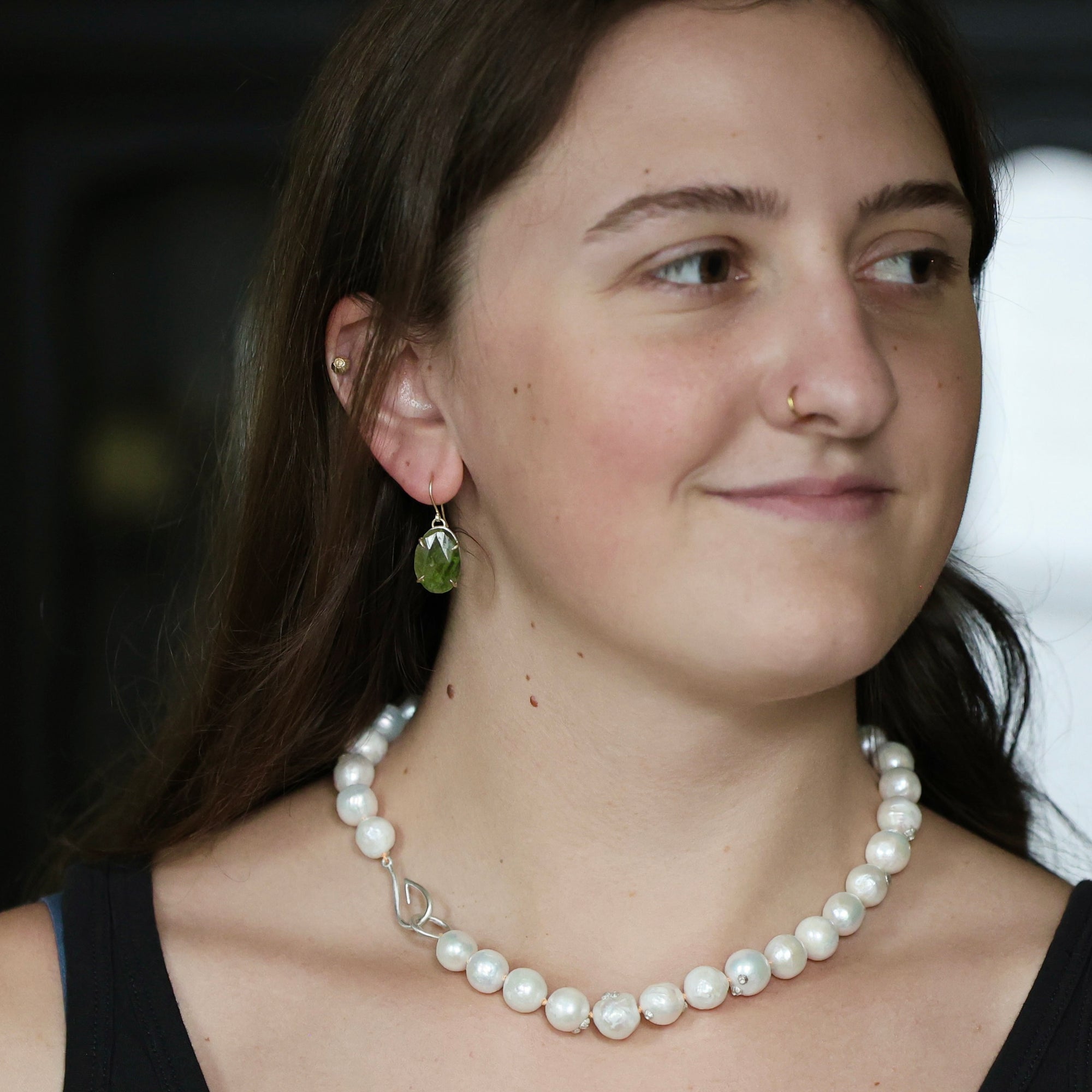 Woman wearing pearl necklace and green drop earrings. 
