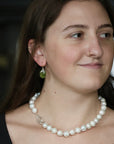 Woman wearing pearl necklace and green drop earrings. 