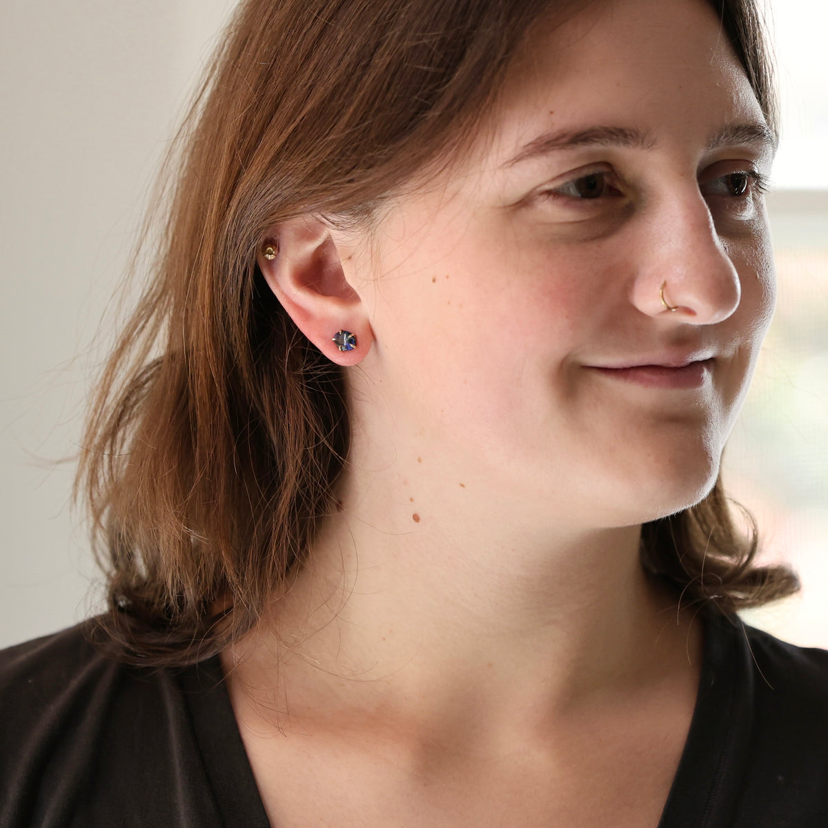 Woman wearing opal studs against a plain background