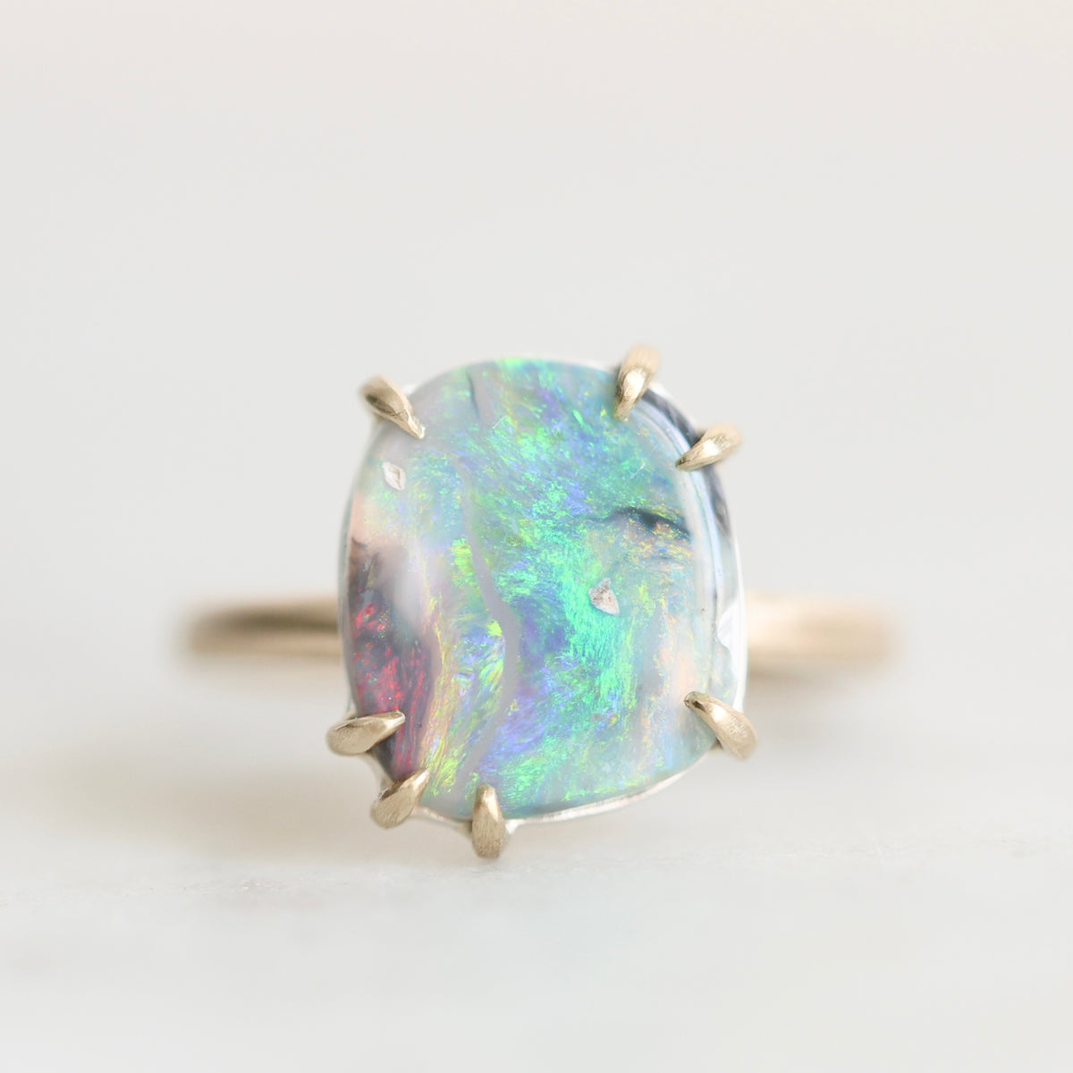 Opal ring set in gold prongs. The opal is colorful with flashes of green, blue, yellow, and pink. 