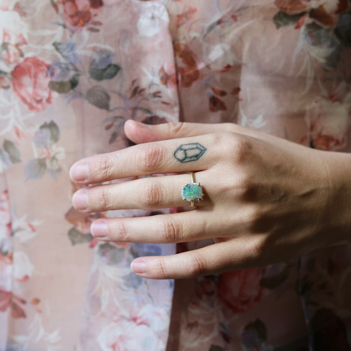 Hand wearing bright opal prong ring against a floral shirt.