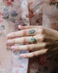 Hand wearing bright opal prong ring against a floral shirt.