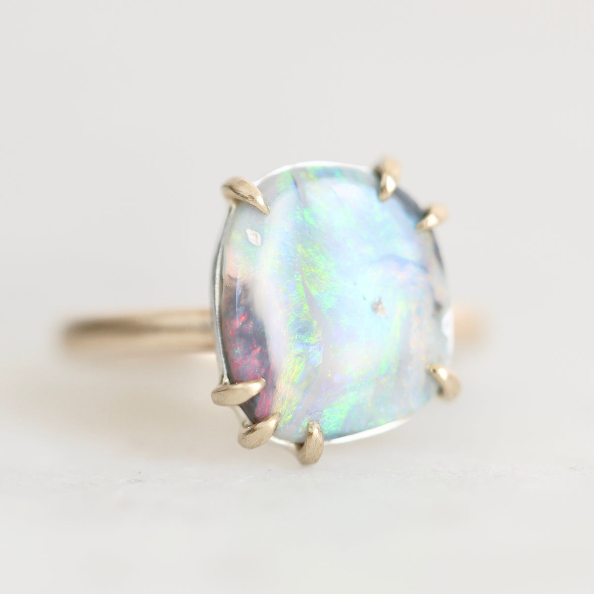 Colorful opal ring with gold prongs against a plain background. 