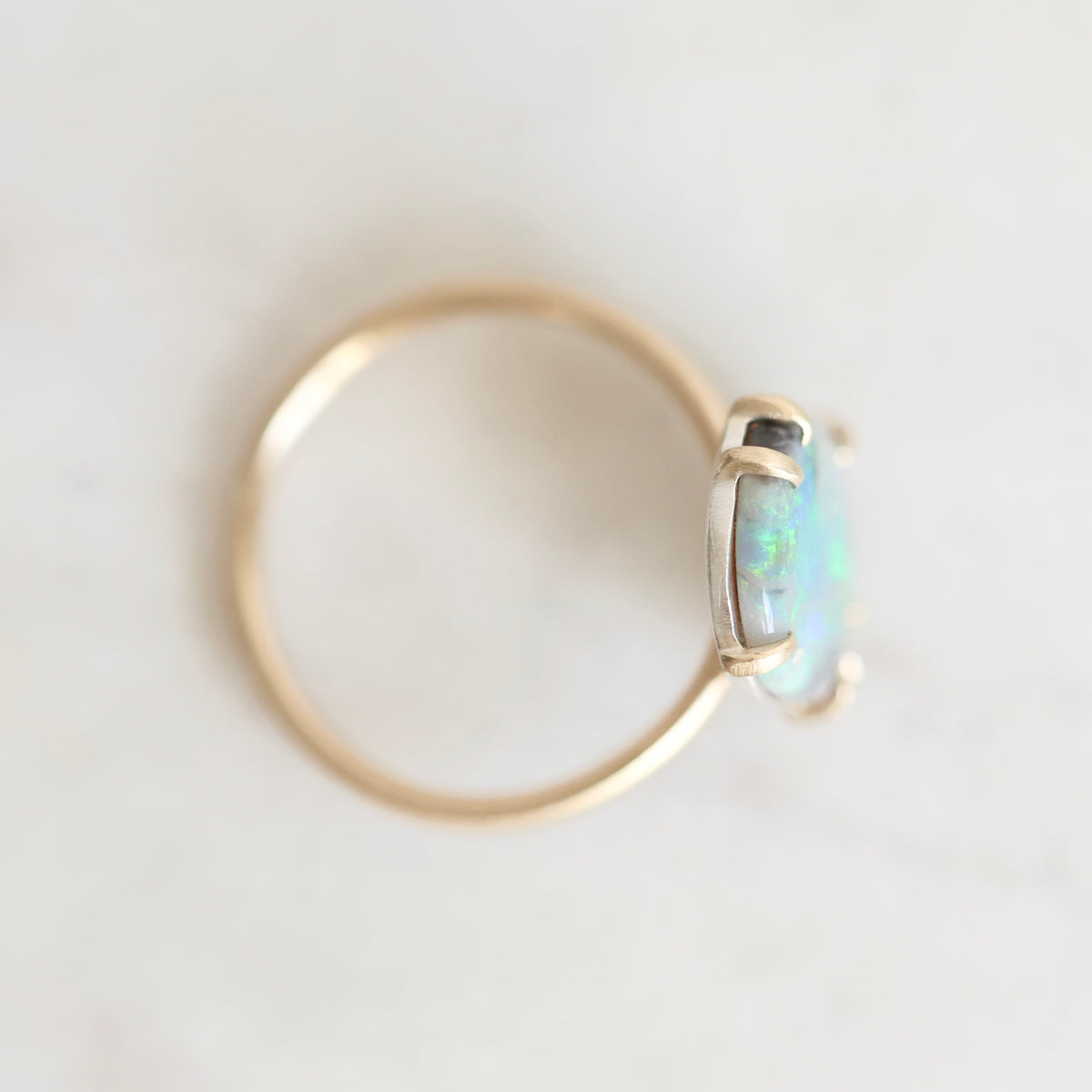 Top down view of opal ring with gold prongs and band against a plain white background.