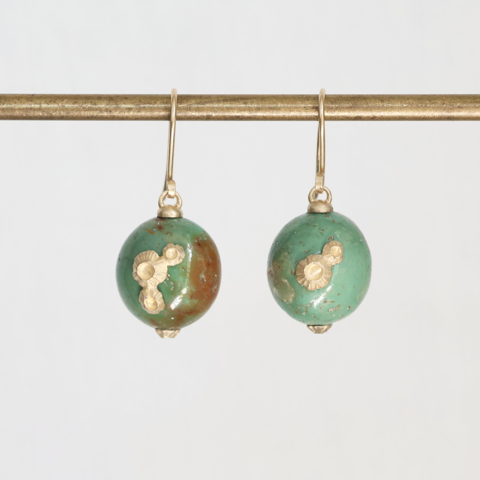 Pair of green earrings with gold accents on a white background