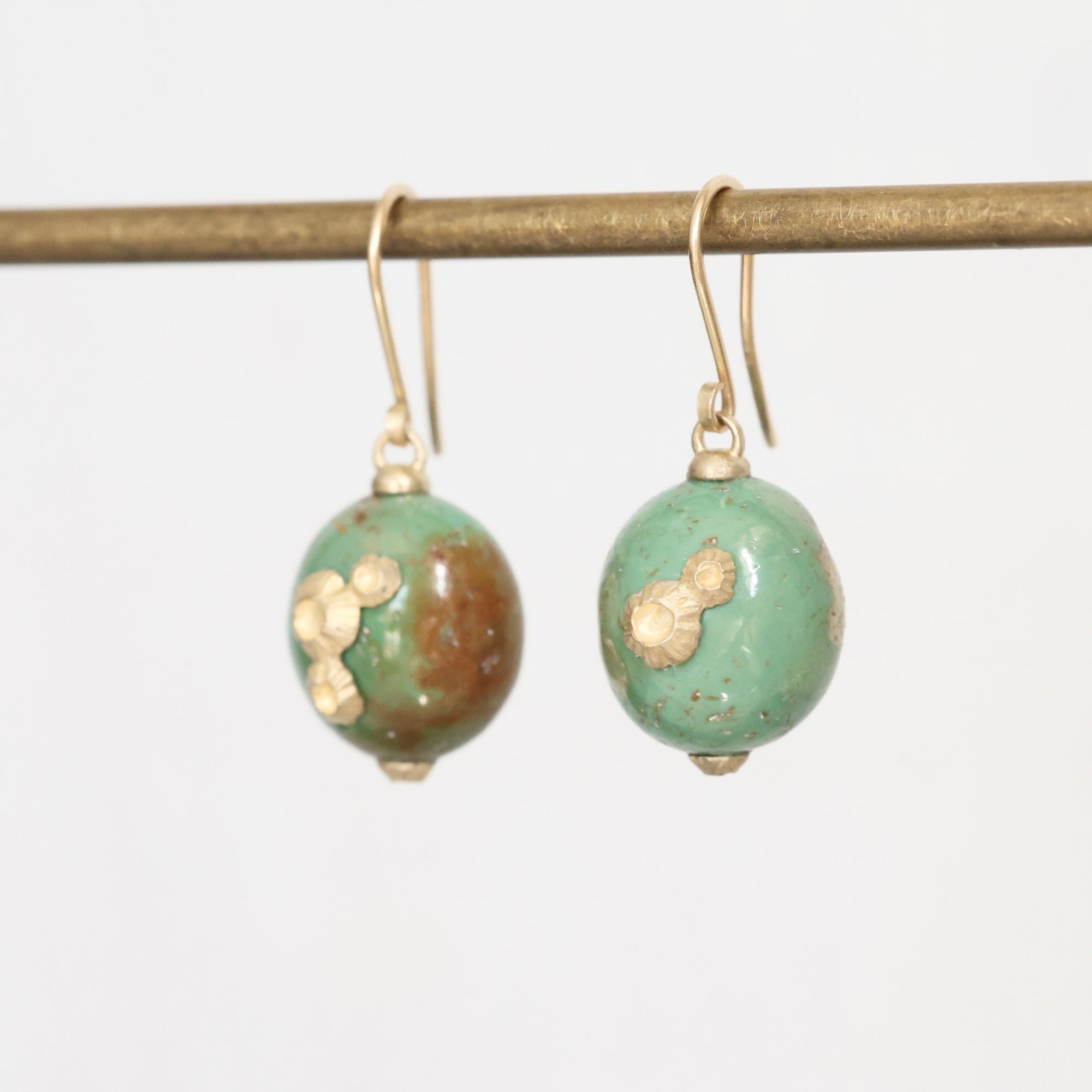 Pair of earrings with green and gold beads on a white background