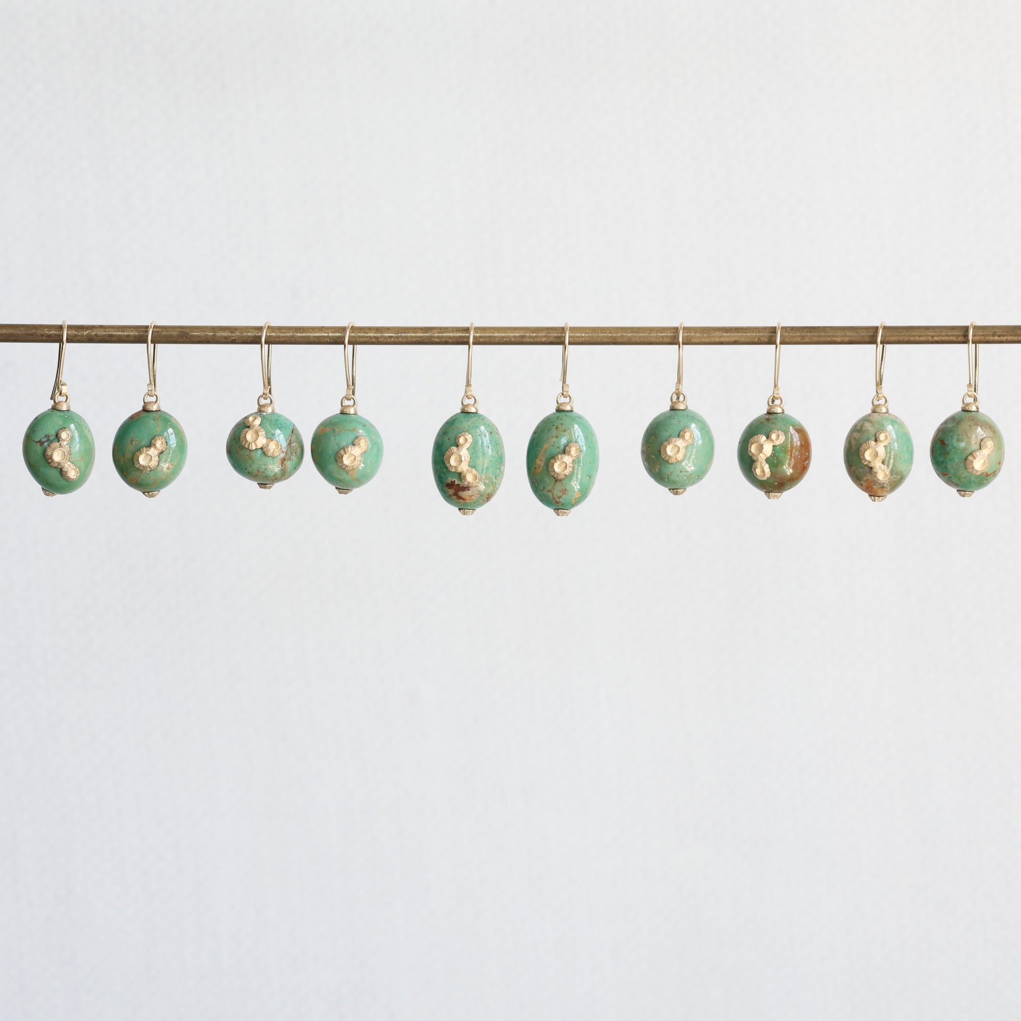 Decorative green eggs with gold accents hanging on a rod against a light blue background